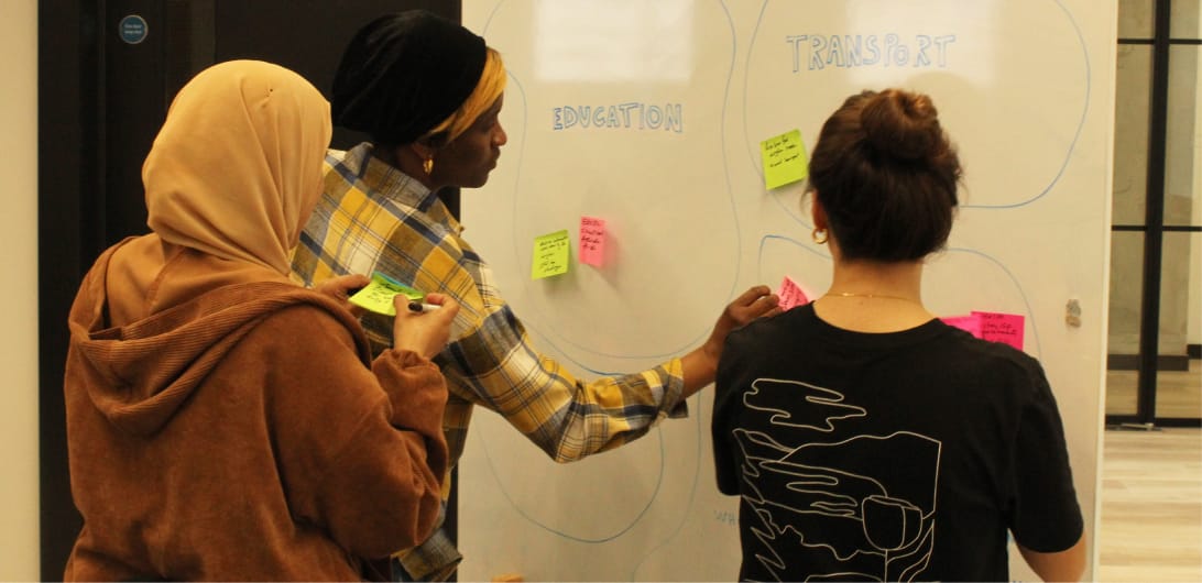 3 people taking part in a workshop in front of a whiteboard with education and transport written on it